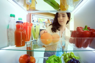 Sağlıklı yiyecek, sebze ve meyvelerle dolu açık buzdolabının yanında duran kadın portresi. Kadın portresi