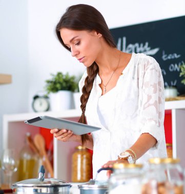 Mutfakta yemek yapmak için tablet bilgisayar kullanan genç bir kadın.