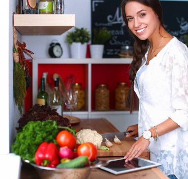 Mutfakta yemek yapmak için tablet bilgisayar kullanan genç bir kadın.