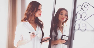 Genç ve güzel bir kadın aynanın yanında makyaj yapıyor.