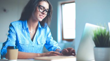 Dizüstü bilgisayar ekranına bakarak office tablosunda oturan genç kadın