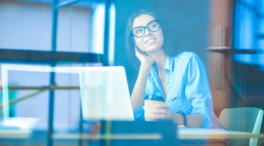 Ofis masasında dizüstü bilgisayarlı genç bir kadın oturuyor, pencereden bakıyor.