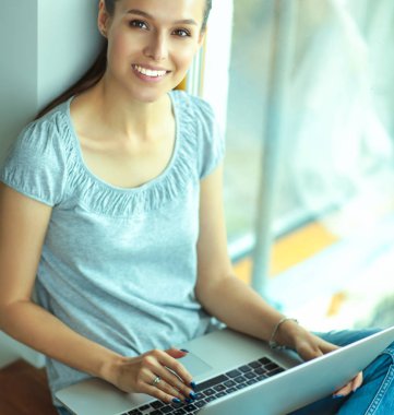 Genç ve güzel bir kadın evde dizüstü bilgisayar kullanıyor.