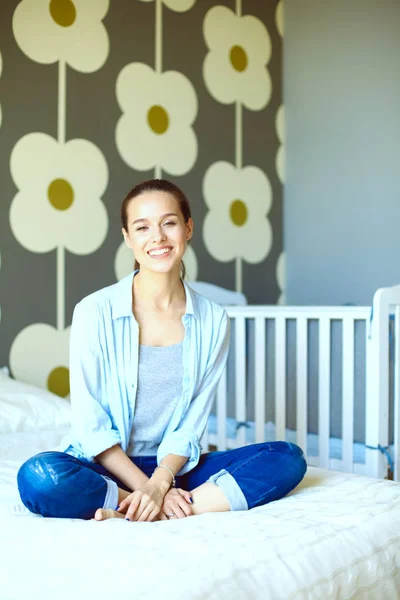 Mladá žena, sedící na posteli v dětské postýlce. Mladá maminka — Stock fotografie