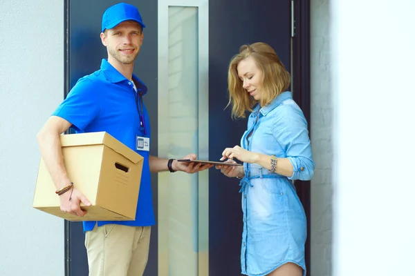 Repartidor sonriente con uniforme azul que entrega la caja de paquetes al destinatario: concepto de servicio de mensajería. Repartidor sonriente en uniforme azul — Foto de Stock