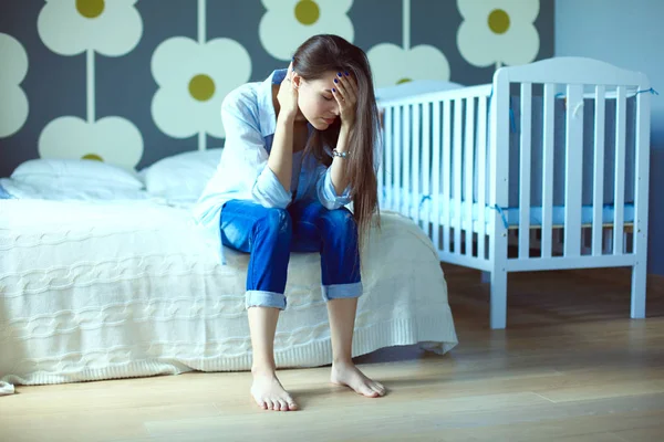 Ung trött kvinna som sitter på sängen nära barnens spjälsäng. Ung mamma. — Stockfoto