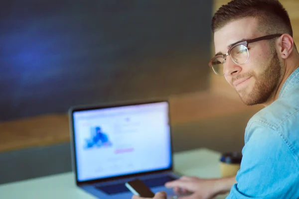 Jonge man met telefoon en werkt op de laptop. — Stockfoto