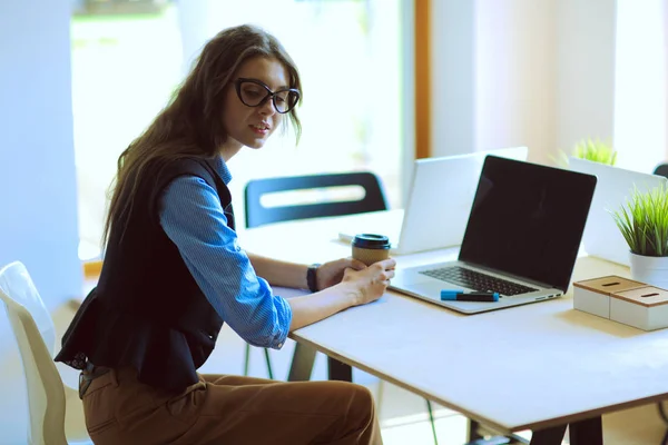 Egy fiatal nő ül az irodai asztalnál laptoppal. Fiatal nő. Laptop — Stock Fotó