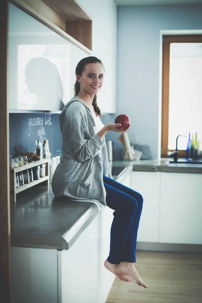 Mulher usando telefone celular sentado na cozinha moderna . — Fotografia de Stock