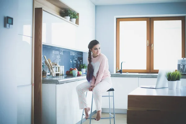 Jovem mulher sentada na mesa na cozinha . — Fotografia de Stock
