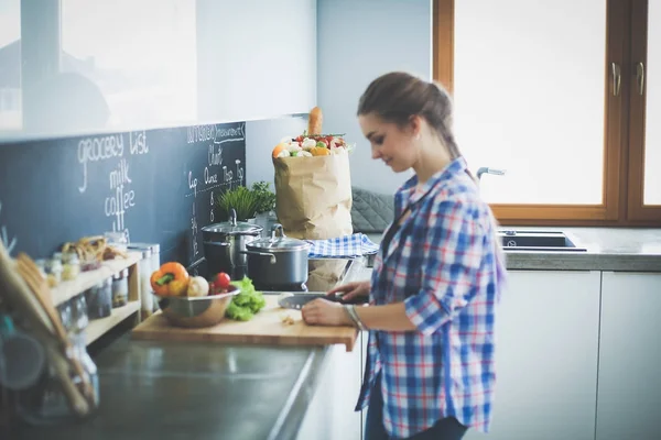 Ung kvinna skära grönsaker i köket nära skrivbordet. — Stockfoto