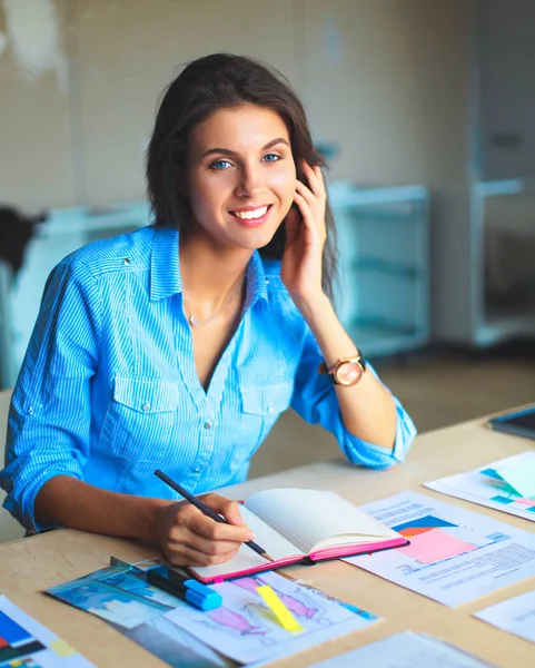 Jeune femme assise au bureau avec instruments, plan et ordinateur portable — Photo