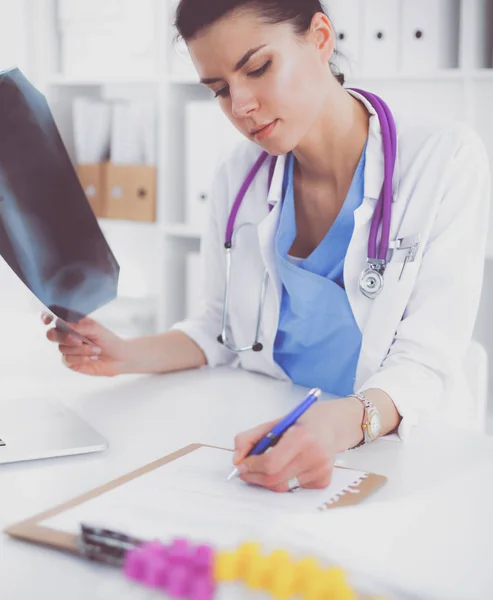 Молодая женщина-врач изучает рентгеновское изображение, сидя на столе — стоковое фото