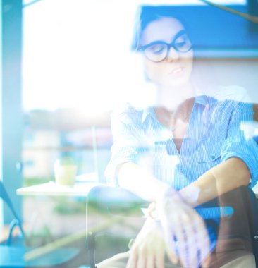 Ofis masasında dizüstü bilgisayarlı genç bir kadın oturuyor, pencereden bakıyor.
