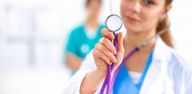 Steteskopu dinleyen genç bayan doktor hastanede duruyor.