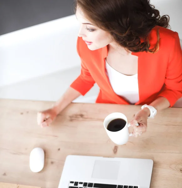 Привлекательная женщина сидит за столом в офисе, работает с ноутбуком — стоковое фото