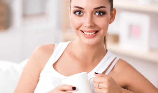 Junge schöne Frau mit einer Tasse auf dem Sofa zu Hause — Stockfoto