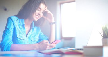 Ofis masasında dizüstü bilgisayarıyla oturan genç bir kadın.