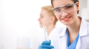 Kadın araştırmacı, beyaz arka planda izole edilmiş ilaç şişeleri ve mataralarla çevrili.