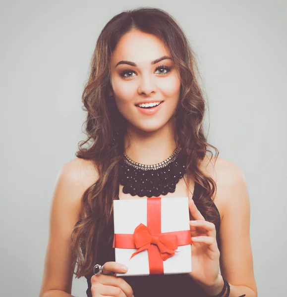 年轻女人幸福的微笑举行礼品盒在手中，在灰色的背景中分离 — 图库照片