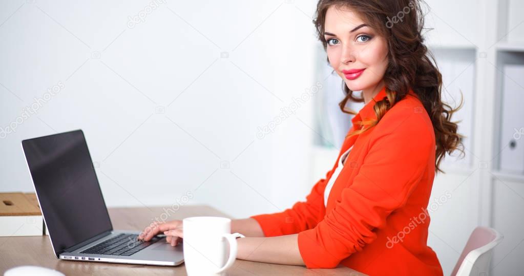 Attractive woman sitting at desk in office, working with laptop computer