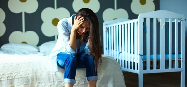 Young tired woman sitting on the bed near childrens cot — Stock Photo, Image