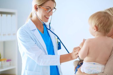 Kadın doktor, klinikte steteskoplu bir çocuğu dinliyor.