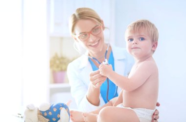 Kadın doktor, klinikte steteskoplu bir çocuğu dinliyor.