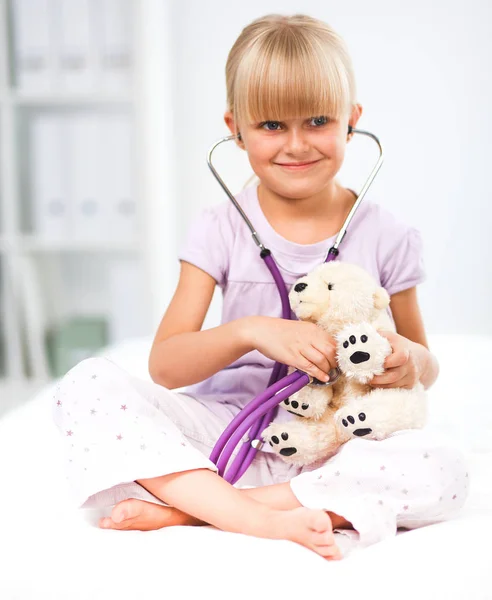 Niña está examinando su osito de peluche usando estetoscopio — Foto de Stock