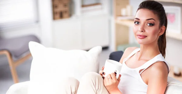 Portret van jonge mooie vrouw met een kop op sofa thuis — Stockfoto