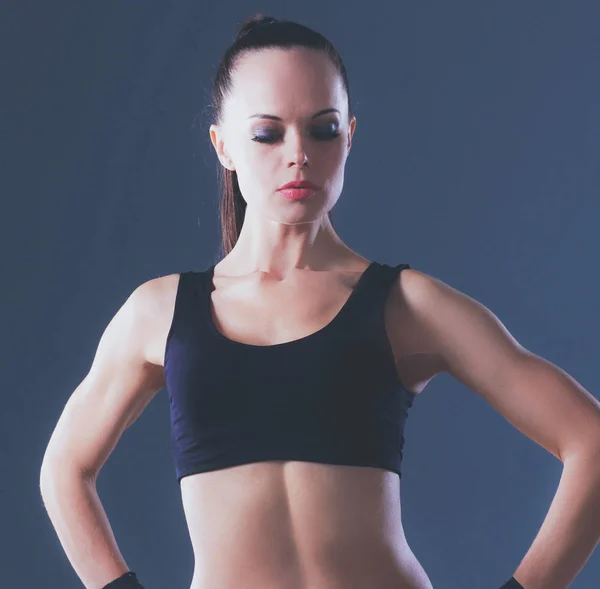 М'язиста молода жінка стоїть на сірому фоні — стокове фото