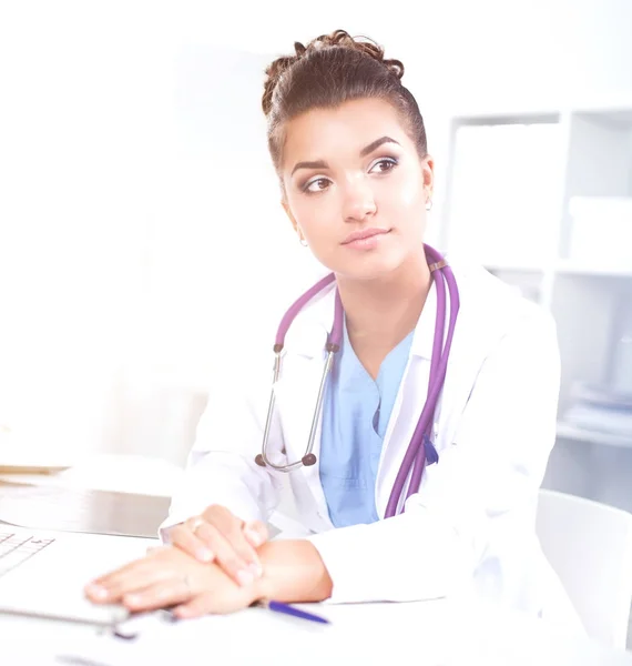 Bonito jovem sorridente médico feminino sentado na mesa e escrevendo. — Fotografia de Stock