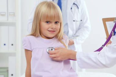 Kadın doktor ameliyatta steteskopla çocuğu muayene ediyor.