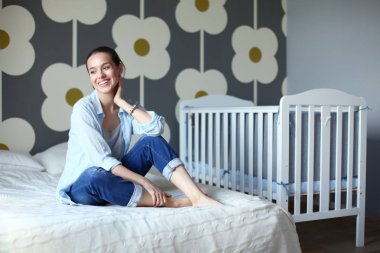 Yatakta çocuk karyolası yakın oturan bir genç bayan. Genç anne