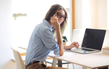 Ofis masasında dizüstü bilgisayarla oturan genç bir kadın. Genç bir kadın. Dizüstü bilgisayar