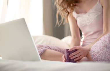 Dizüstü bilgisayar ile yatakta oturan genç güzel kadın.