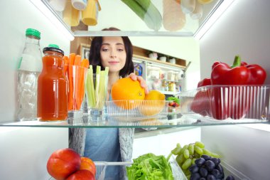 Sağlıklı yiyecek, sebze ve meyvelerle dolu açık buzdolabının yanında duran kadın portresi. Kadın portresi