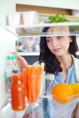 Sağlıklı yiyecek, sebze ve meyvelerle dolu açık buzdolabının yanında duran kadın portresi. Kadın portresi