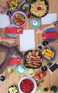 Ahşap masada otururken birlikte yemek yiyen bir grup insanın üst düzey görüntüsü. Masada yemek var. İnsanlar fast food yiyor..