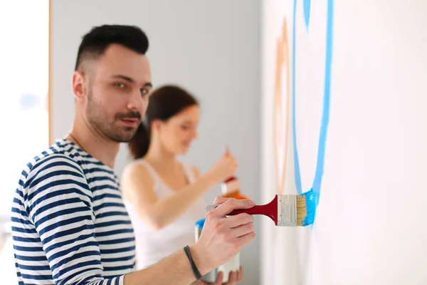 Porträtt av glada leende unga par målning interiör vägg i nytt hus. unga par — Stockfoto