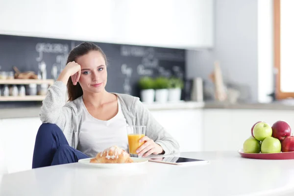 Ung kvinna med apelsinjuice och tablett i köket. — Stockfoto