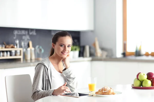 Ung kvinna med apelsinjuice och tablett i köket. — Stockfoto