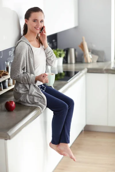 Kvinna med mobiltelefon sitter i moderna kök. — Stockfoto