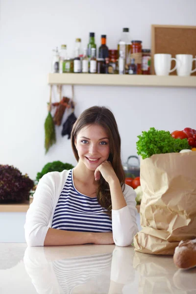 Ung kvinna som håller livsmedelsbutiker shoppingväska med grönsaker. Stående i köket. Ung kvinna — Stockfoto