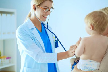 Kadın doktor, klinikte steteskoplu bir çocuğu dinliyor.