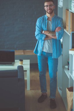 Duvarın yanında dizüstü bilgisayar tutan genç adam..