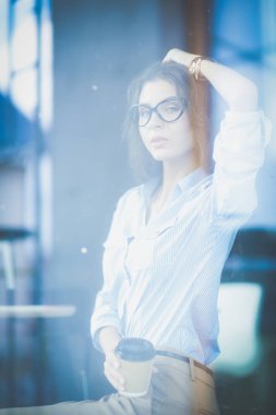 Ofis masasında dizüstü bilgisayarıyla oturan genç bir kadın. Pencereden bakıyor. Genç kadın.