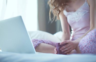 Dizüstü bilgisayar ile yatakta oturan genç güzel kadın.