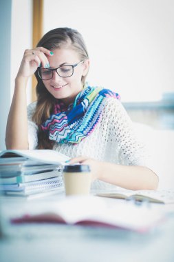 Kitapların arasında bir masada oturan genç bir kadın. Öğrenci