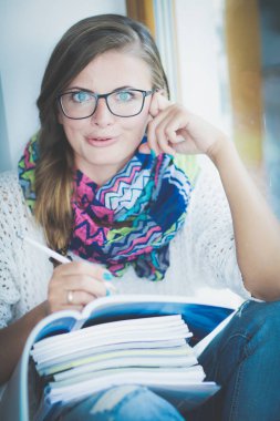 Kitapların arasında bir masada oturan genç bir kadın. Öğrenci